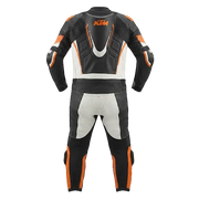 A black, white, and orange leather racing suit shown from the back, featuring protective padding and the  logo on the upper back, set against a plain white background with a circular brand badge in the top right corner.